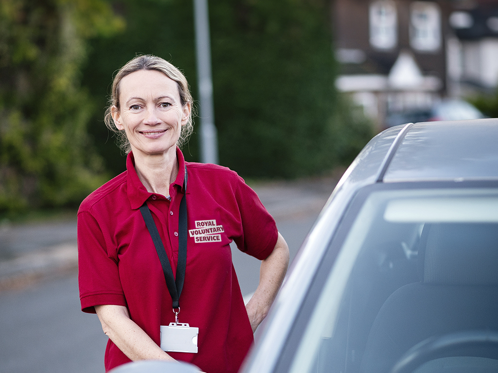 A Royal Voluntary Service Volunteer standng in front of a car 