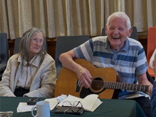 Royal Voluntary Service dementia support group member playing guitar with his wife, who lives with dementia, at a Birmingham group