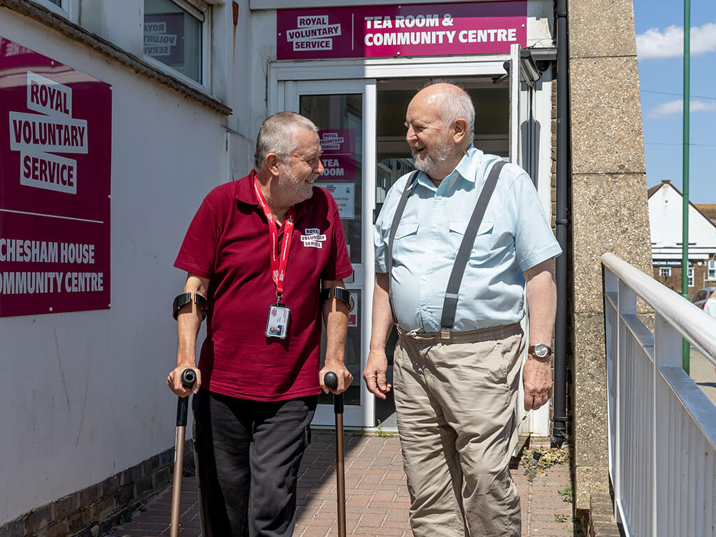 A volunteer, walking with the aid of sticks, with a client outside our community hub, Chesham House in Lancing. 