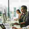 A man in an office sat at a work desk looking at a computer screen 