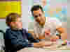 A younger volunteer supporting a younger boy while both looking at a colouring book