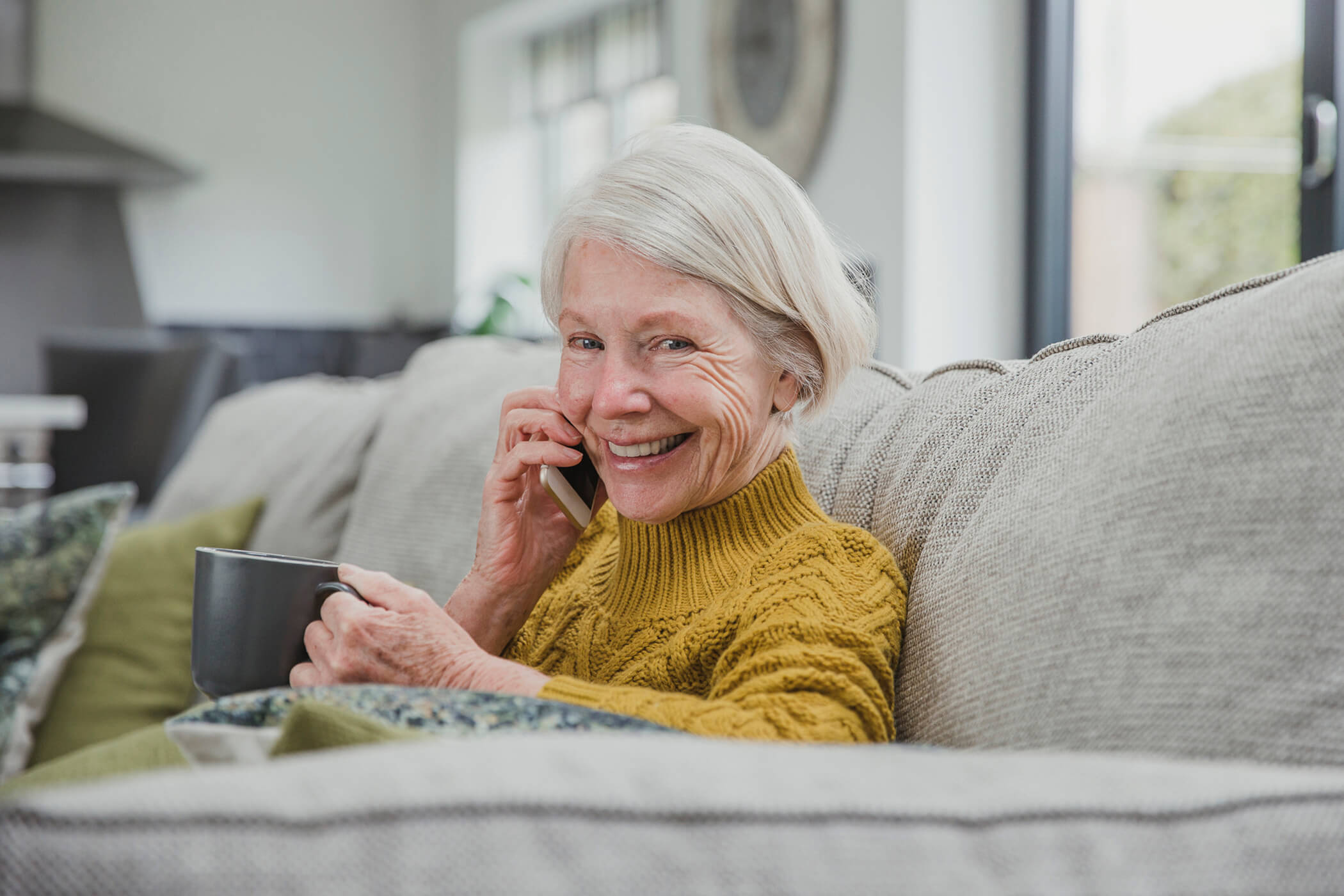 An older woman on the phone and enjoying a cup of tea