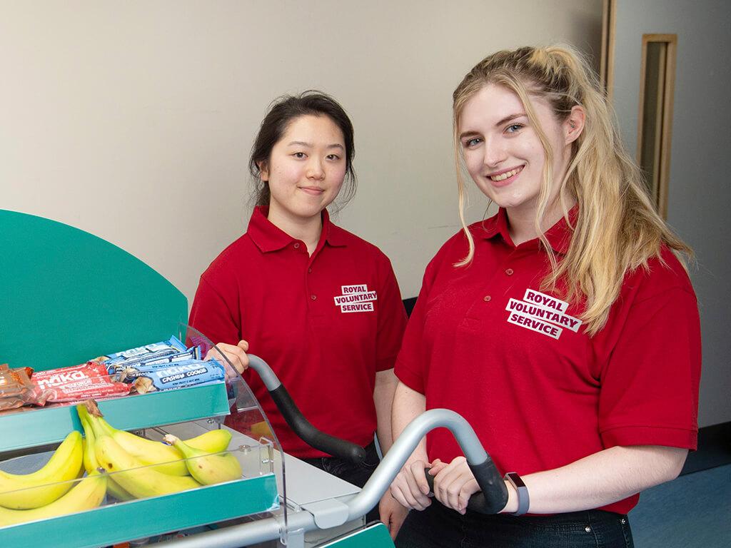 Two volunteers pushing a trolley with snacks and refreshments on a hospital ward 