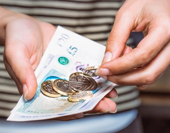 A person holding some cash made up of notes and coins