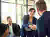 A woman leaning over a desk in a business meeting to shake a colleague's hand 