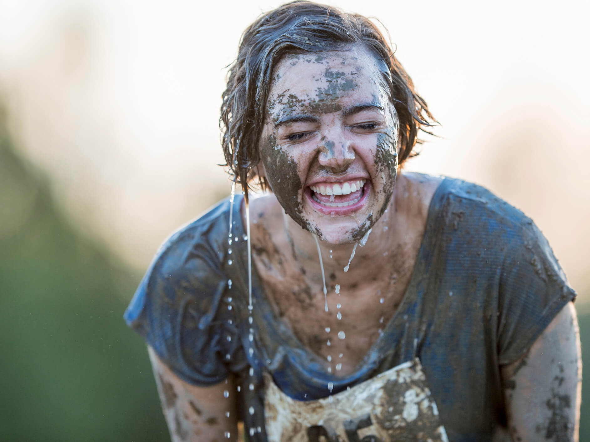 A woman smiling while covered in mud with water dripping from her face on a mud race 