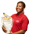 A young woman holding a bag of shopping and smiling wearing a red polo top with the Royal Voluntary service logo