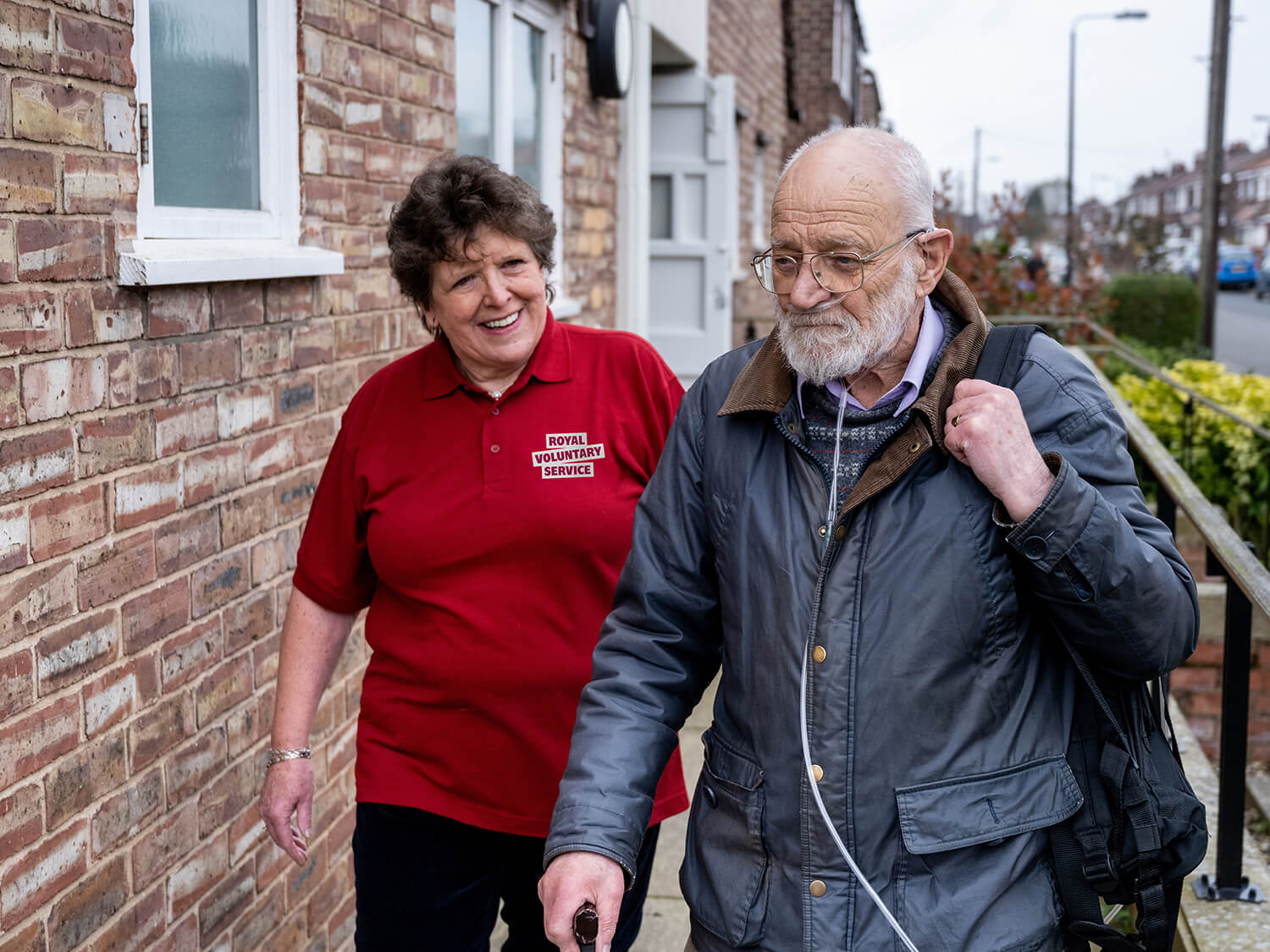 A Royal Voluntary Service volunteer supporting an older man wearing an oxygen mask while on a walk 