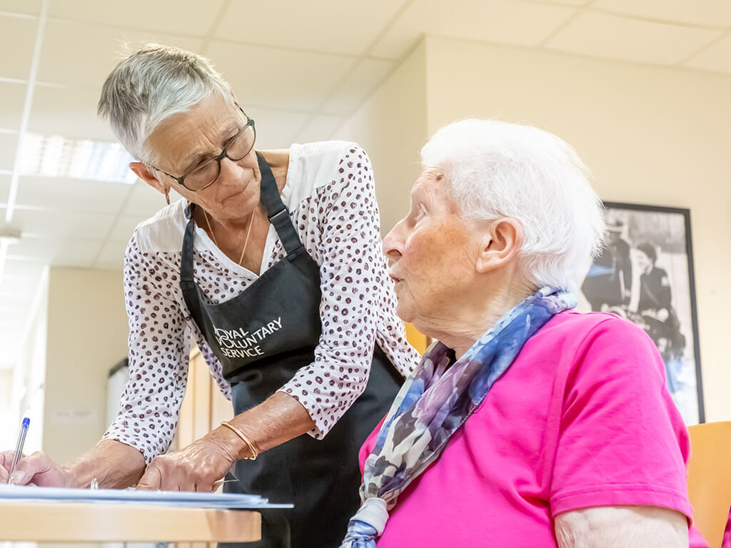 A Royal Voluntary Service volunteer speaking to a client at a lunch club