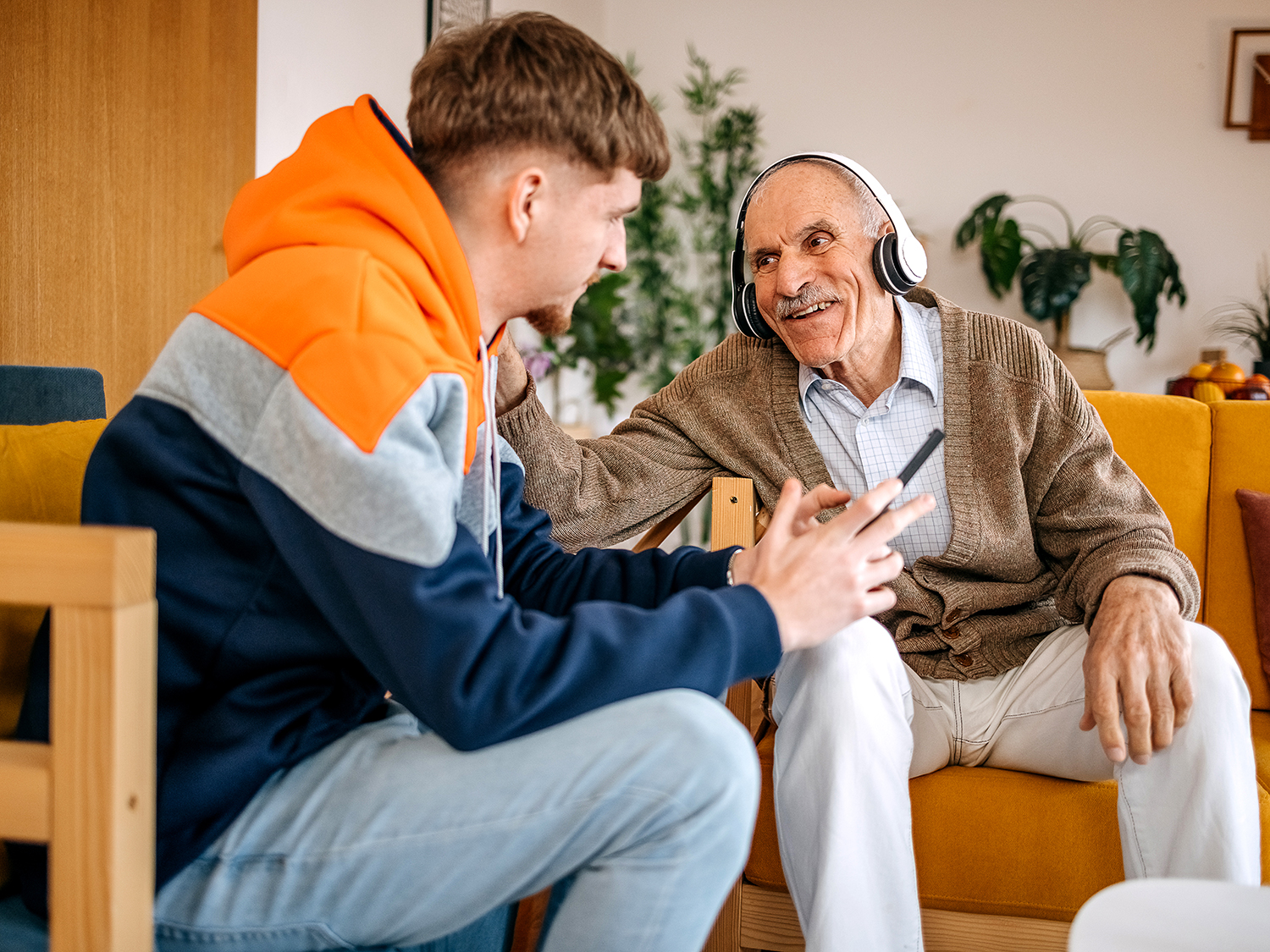 A younger volunteer helping an older man in a pair of headphones with his mobile phone 