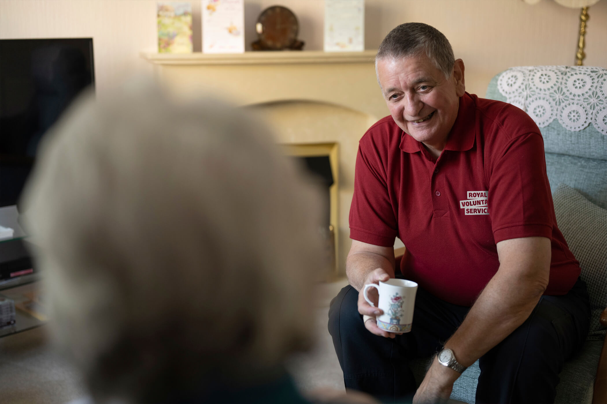 A volunteer enjoying a cup of tea with an older person in a home setting 