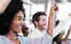 A woman and man at a work meeting raising their hands 