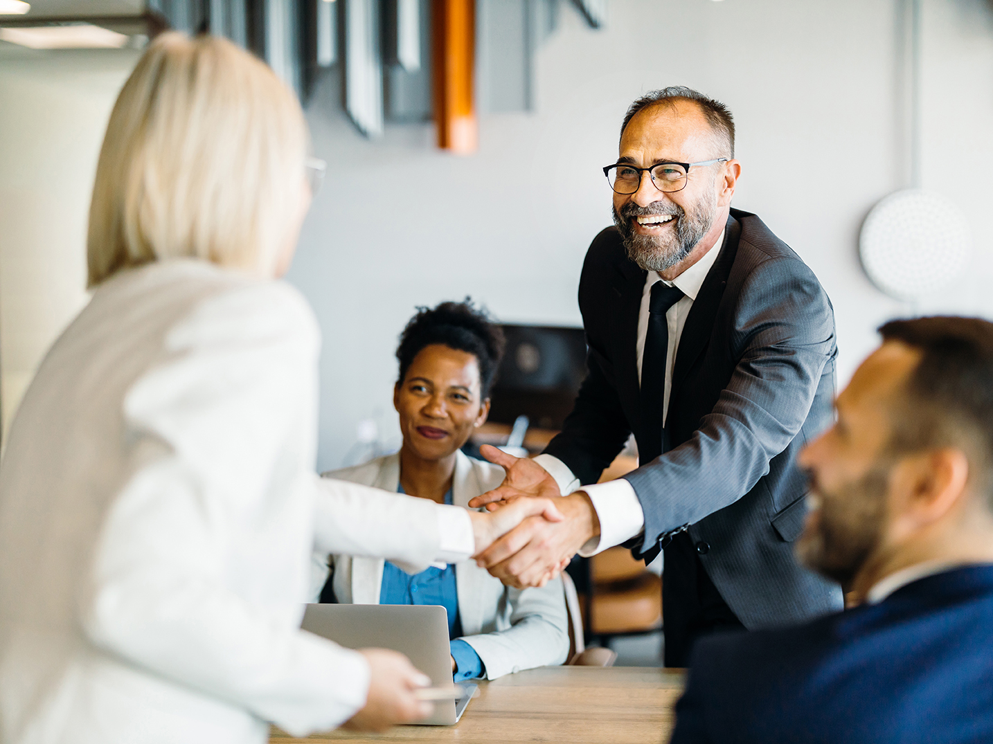A smiling man leaning over a desk to shake someone's hand 