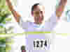 A woman grinning as she crosses the finishing line of a charity fun run 