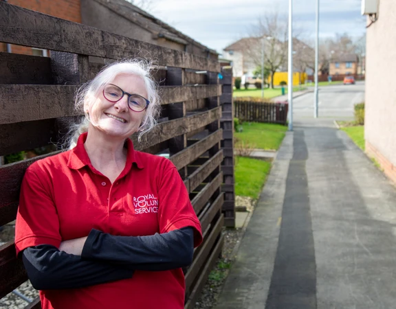 A Royal Voluntary Service volunteer leaning against a fence