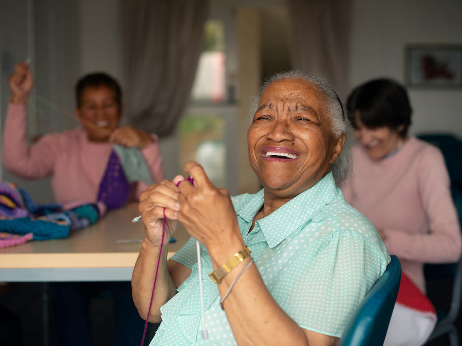 An smiling older woman at a demetia club taking part in a knitting activity session